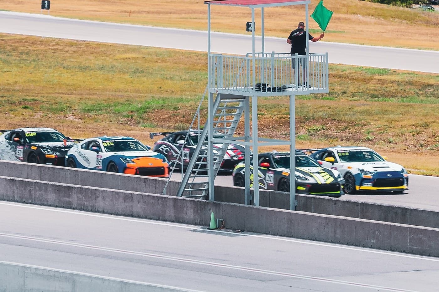 A corner marshal waving the green flag as a full Time Attack grid streams past