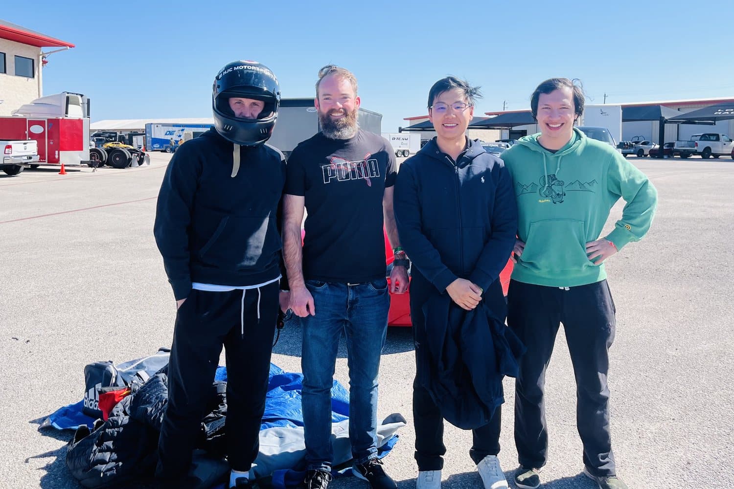 Four drivers in everyday clothes standing together in the paddock at Motorsport Ranch Cresson before a session