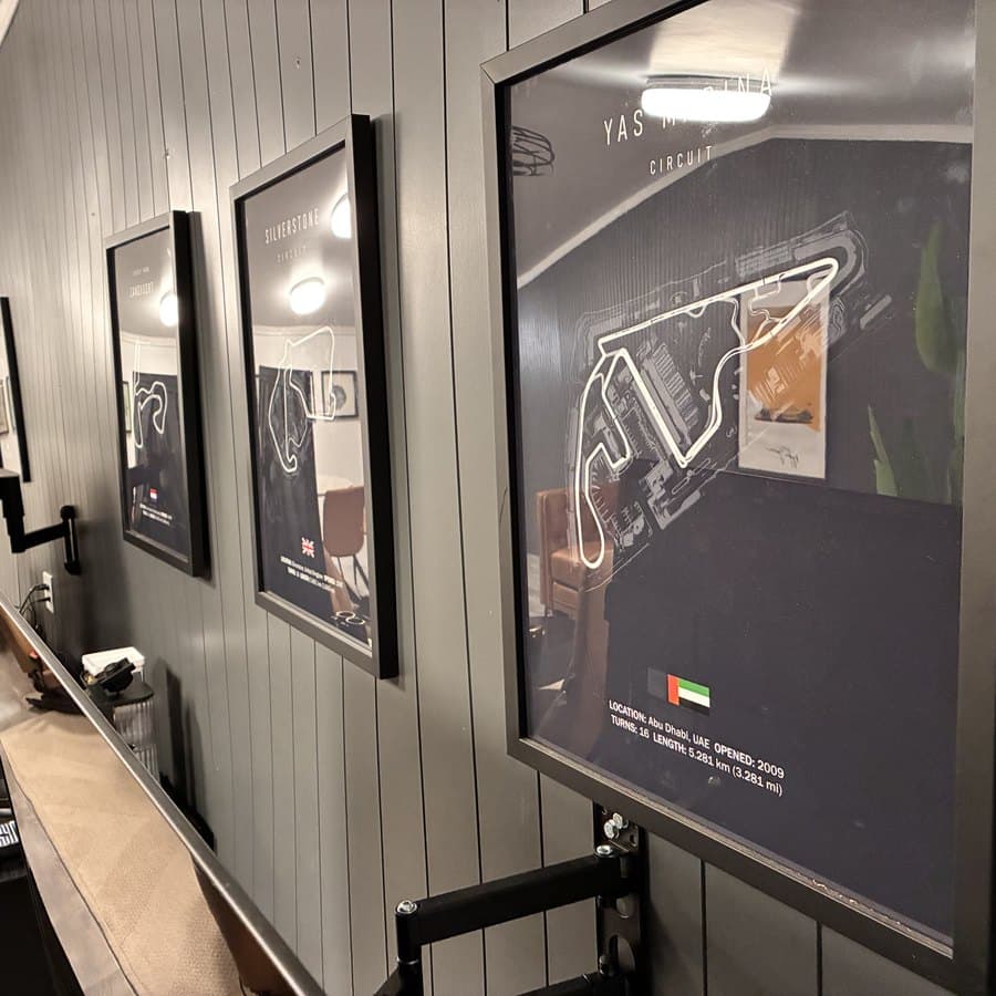 Framed circuit maps lining the wall of Senna's Lounge beside a review monitor